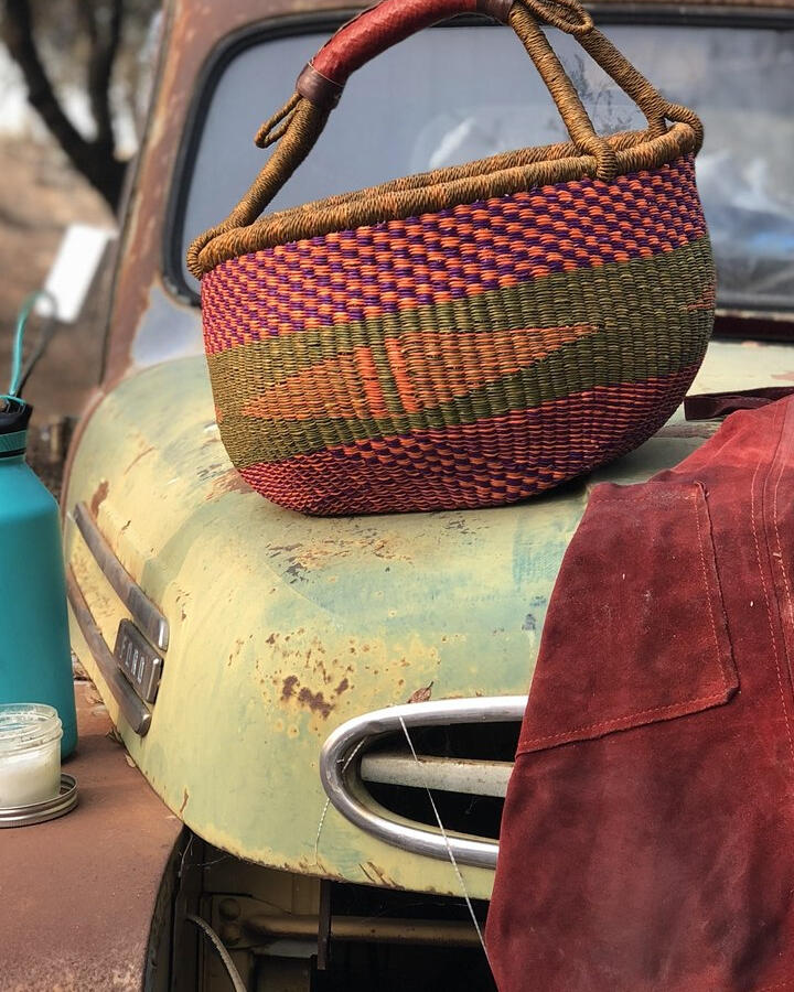 A colorful woven basket and red apron resting on a vintage truck