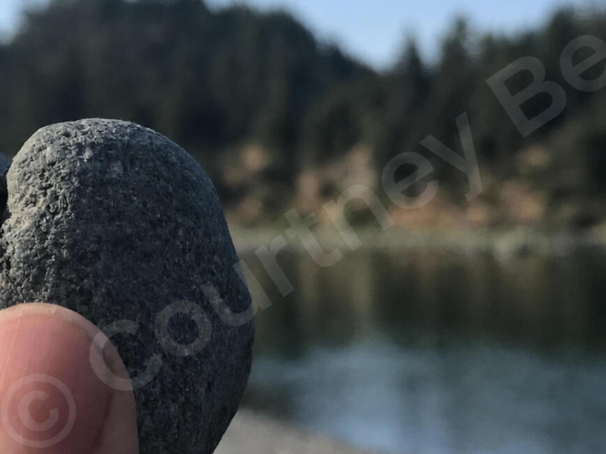 © CourtKnee.B A hand holding a naturally heart-shaped stone beside a quiet river, photographed by Courtney Bee — © CourtKnee.B